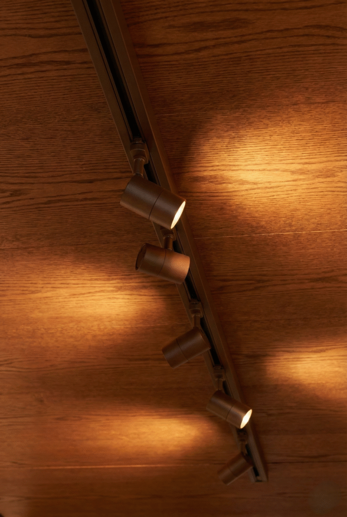 Ceiling-mounted black track channel lights casting warm beams on wooden wall